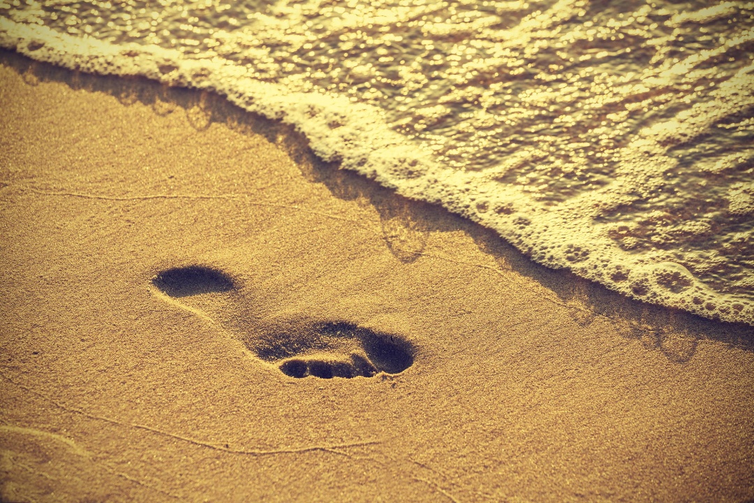 Footprint on sand beach along the edge of sea, vintage retro style.