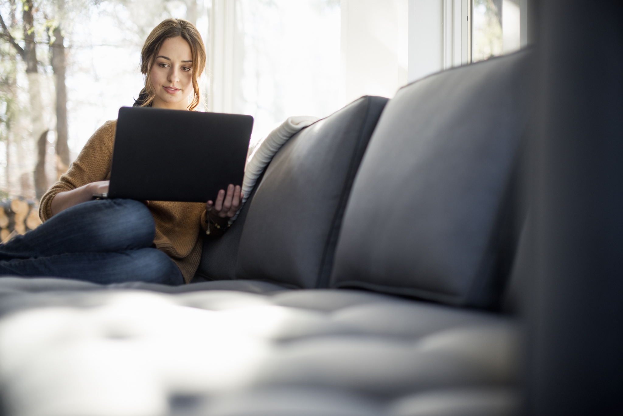 Woman sitting on a sofa looking at her laptop, smiling.