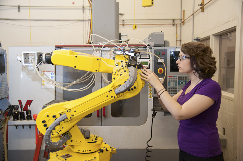 Woman operating yellow robotic arm.