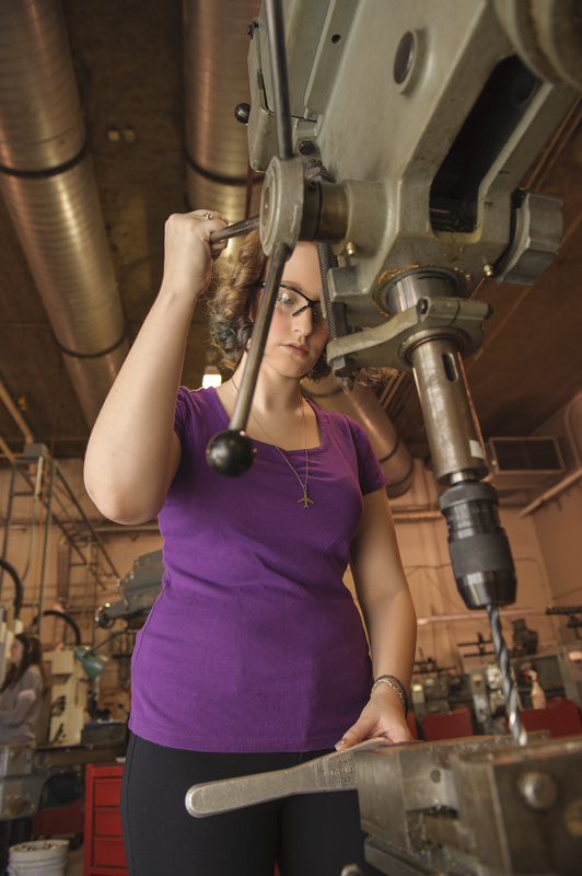 Woman engineer working a drill press machine.