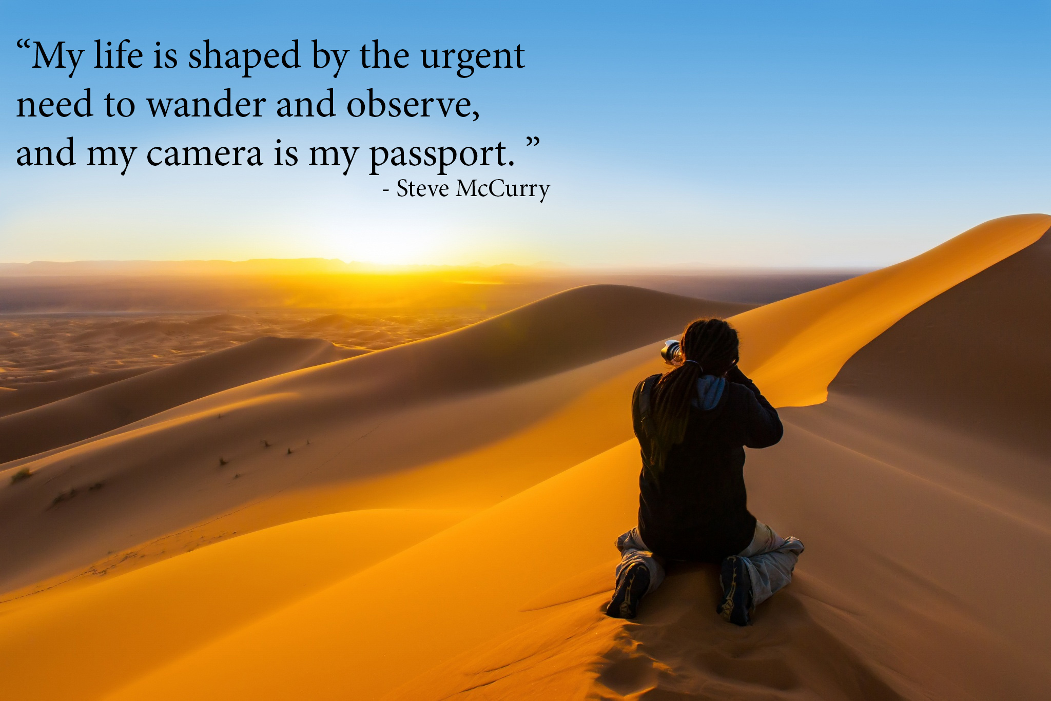 Handsome man with dreadlocks taking a photograph of sunset from a sand dune