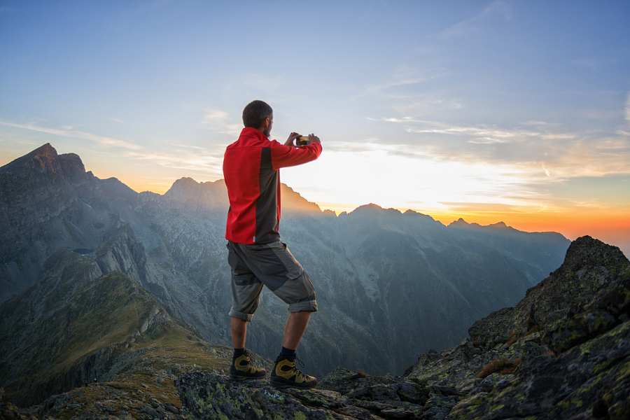 Traveller taking a photo of the sunset over a mountain ridge with his smart phone