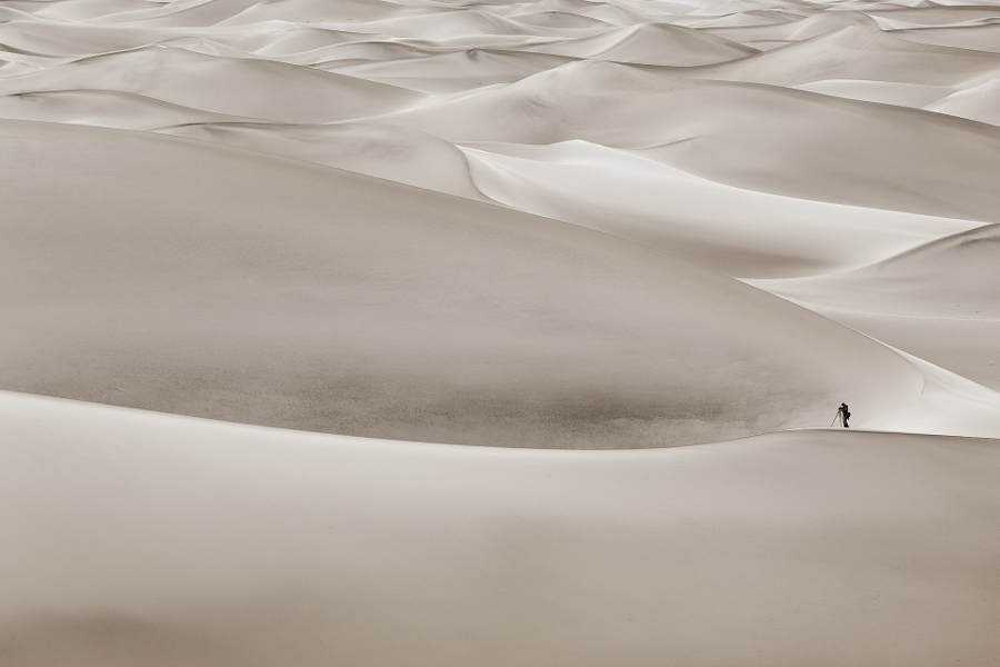A lone photographer stands among the giant dunes of Mequite Dunes in Death Valley National Park, California.