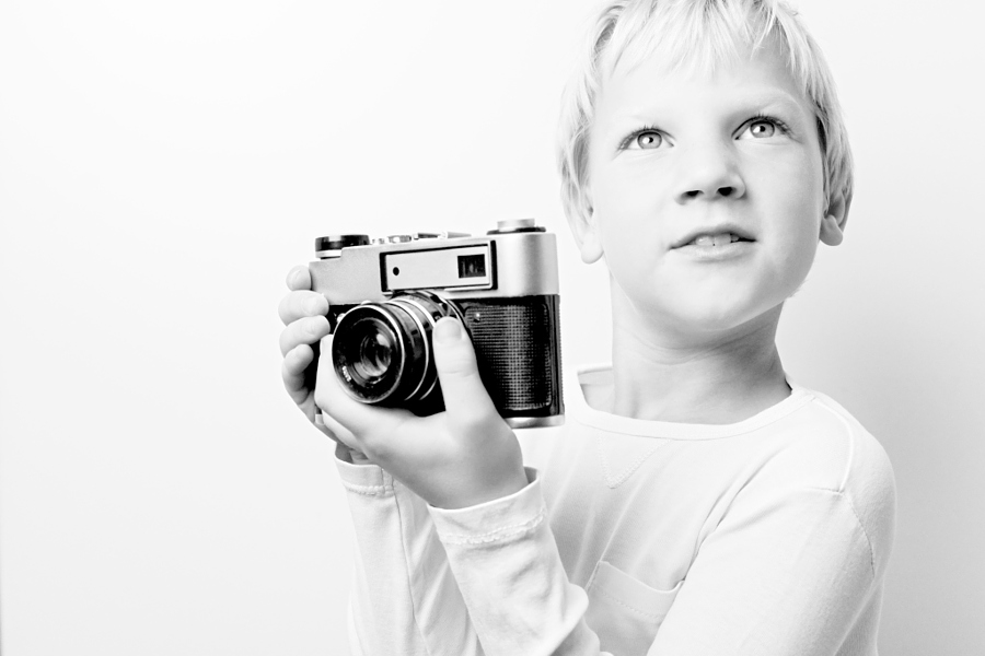 Young 8 year old caucasian blonde haired boy holding retro vintage lomo rangefinder film camera looking for a subject.