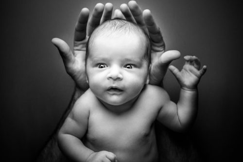 A naked infant being held in his or her parent's hands in