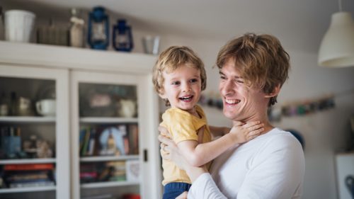 A happy father holding a toddler son at home.