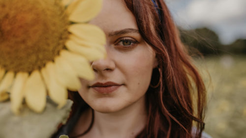 Girl standing in a sunflower field holding a sunflower up to the camera