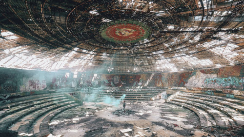 A figure standing in the middle of a large, circular abandoned building