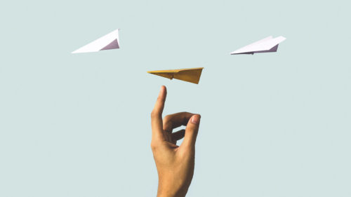 Hand with a finger pointing up at paper airplanes