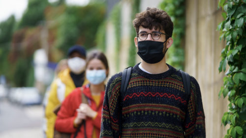 Young people standing in a line outside wearing masks