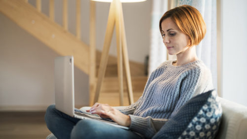 A young woman sitting indoors on a sofa at home, using laptop