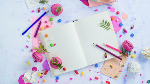 Colorful flat lay with an open book with blank pages, confetti, sweets, hard candy, pink