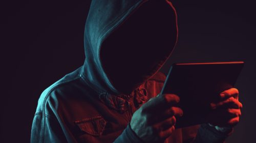 Hooded computer hacker with tablet computer