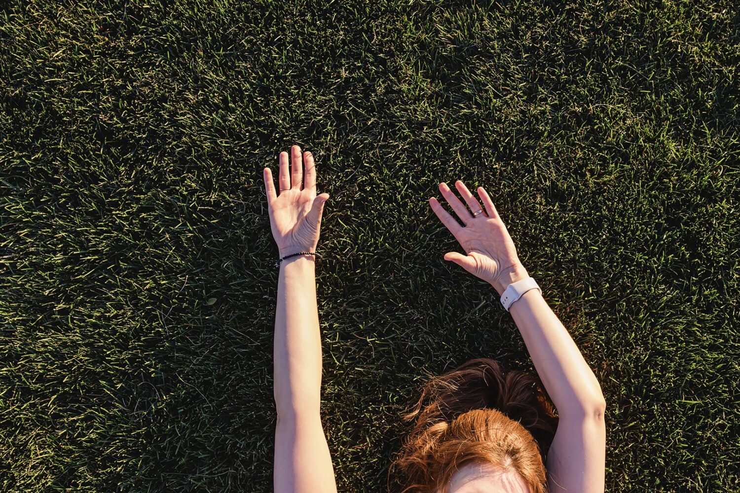 Unrecognizable woman lying on the green grass with her hands raised By Diana Vyshniakova 2