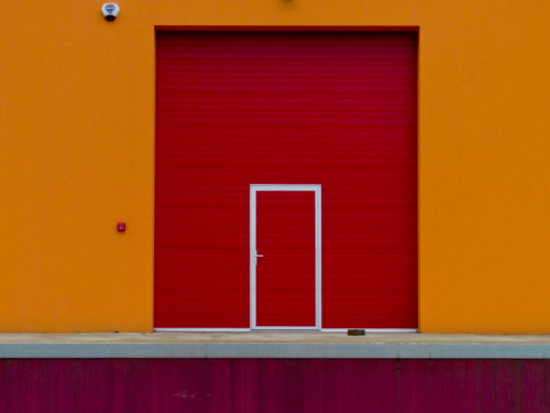 A bold architectural shot of a red door framed by an orange wall, showcasing harmonious analogous color schemes.