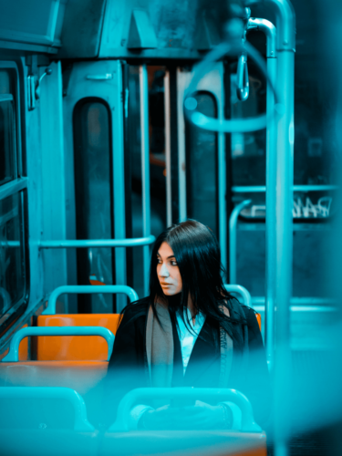 A woman sits alone on a bus with striking blue lighting and orange seats, highlighting color blocking in photography through contrasting tones.