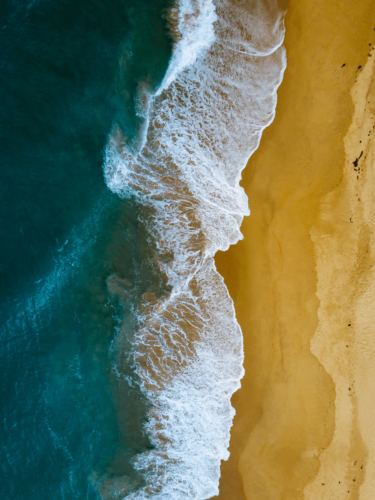 Aerial view of turquoise ocean waves crashing against golden sand, capturing the essence of vibrant photography through striking natural contrast.