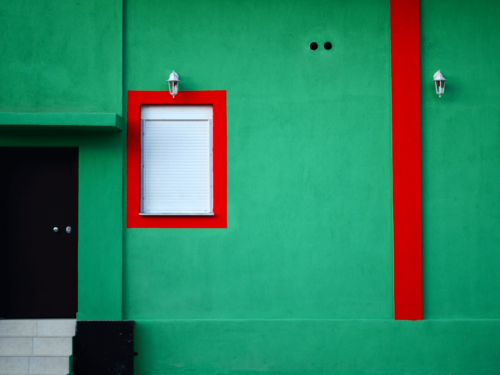 A green building facade with bold red accents and white window shutters, showcasing vibrant photography through strong complementary colors.
