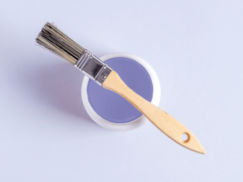 A minimal flat lay of a wooden paintbrush resting on a can of purple paint, illustrating monochrome photography with soft tonal consistency.