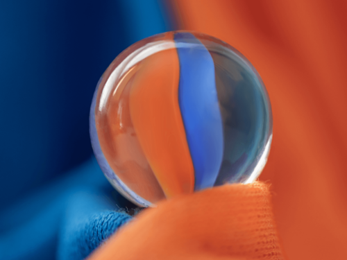 Close-up of a glass marble resting on vivid orange and blue fabric, illustrating vibrant photography with rich textures and bold complementary colors.