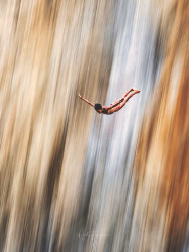 A diver mid-air in front of a blurred waterfall, emphasizing motion and direction through the panning technique.
