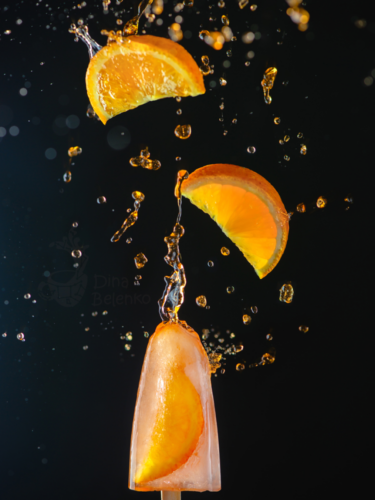 A frozen moment of orange slices and liquid splashing around a popsicle, captured using burst photography to highlight motion in a vivid, dynamic scene.