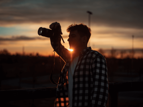 A backlit portrait of a man holding a camera against a vibrant sunset, showcasing the dramatic tones of golden hour portraits.