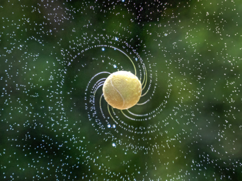 A tennis ball spinning in mid-air with droplets spiraling outward, dramatically captured using burst photography to emphasize motion and energy.