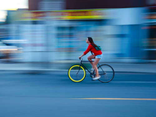 A woman riding a bicycle with a colorful wheel, captured with motion blur to emphasize her speed through an urban setting.
