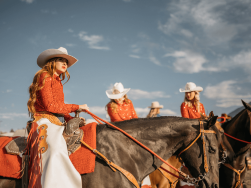 Group of women in cowboy hats riding horses in a parade under clear skies, captured in midday sunlight photography.