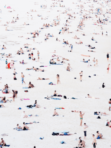 Crowded sandy beach filled with sunbathers and groups of people enjoying the day, an example of creative use of sunlight in photography.