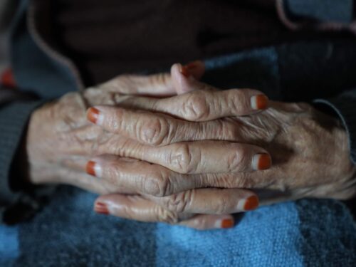Close-up of an elderly woman’s clasped hands with henna-stained nails, symbolizing age, tradition, and resilience.