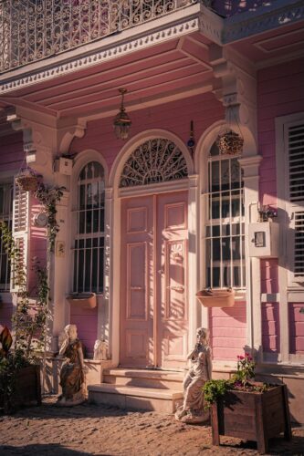 Charming pink house facade with statues and ornate details, photographed by Tu?ba Din showcasing architectural beauty and warm tones.