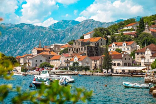 Scenic coastal village with boats on turquoise water and mountains in the background, photographed by Tu?ba Din.