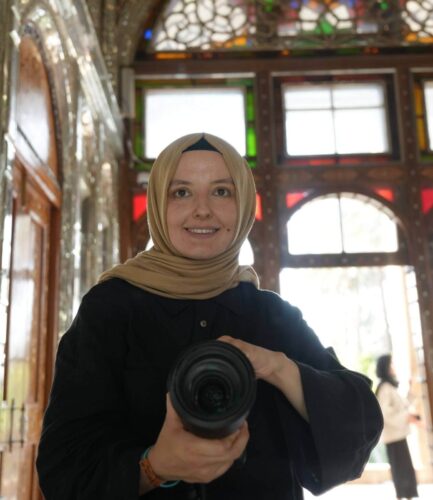 Tu?ba Din holding a camera inside a historic building with colorful stained glass windows.