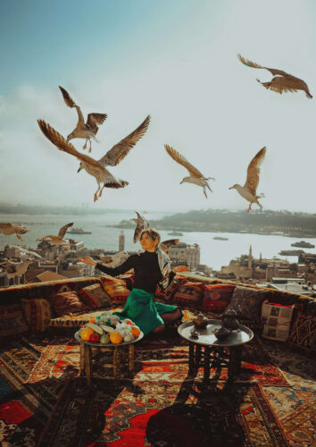 A finalist entry in the 2025 OnePlus Photography Awards showing a woman seated on a rooftop with seagulls flying overhead, overlooking a city and river view.