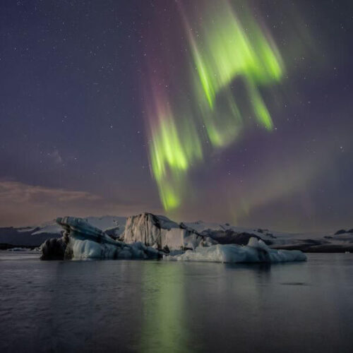 Winning photo from the 2025 OnePlus Photography Awards showing the northern lights glowing above icy mountains and water.