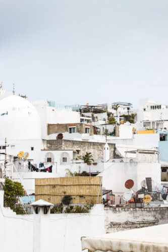 Cluster of whitewashed buildings with domed rooftops and satellite dishes under a pale sky, photographed by Maggie Gongolevich.
