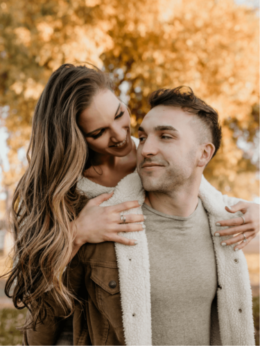 Soulful seasonal portraits of a couple sharing a joyful moment outdoors during fall, surrounded by warm golden foliage.
