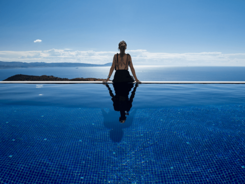 A woman sits at the edge of an infinity pool overlooking a vast blue ocean, with cool-toned color grading enhancing the emotional impact through calm, serene hues.