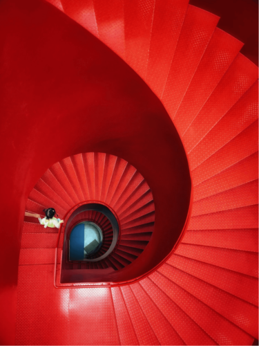 A vibrant red spiral staircase viewed from above, with bold color grading for emotional impact, emphasizing intense reds and graphic, swirling lines.