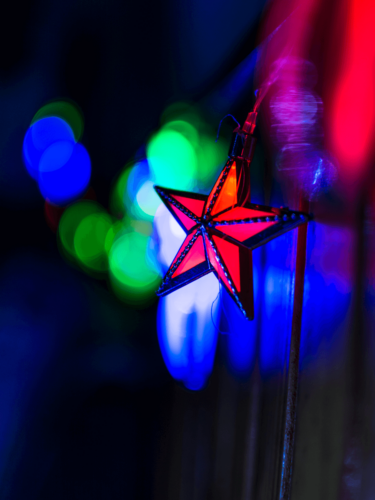 A red star ornament hanging against vibrant blue and green bokeh lights, showcasing bokeh techniques for festive photography.