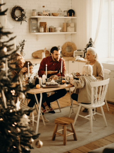 A multigenerational family gathered around a rustic dining table for a holiday meal, sharing food and conversation in a warm, tradition-filled home.