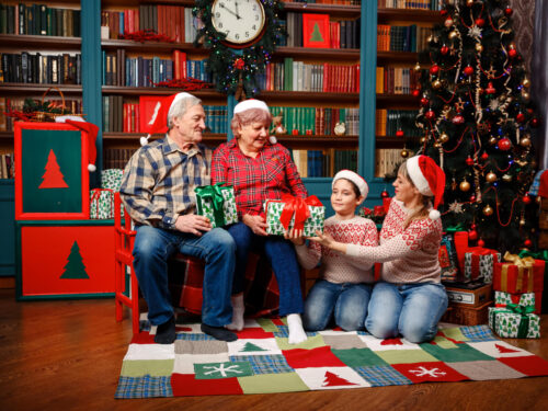 Grandparents and grandchildren exchanging wrapped Christmas gifts in a festive living room decorated with a tree, lights, and presents, representing cherished family traditions.