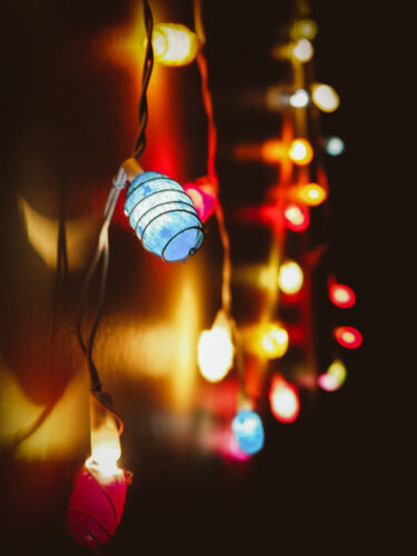 Close-up of multicolored string lights on a dark background, captured with bokeh techniques to create soft glowing circles.