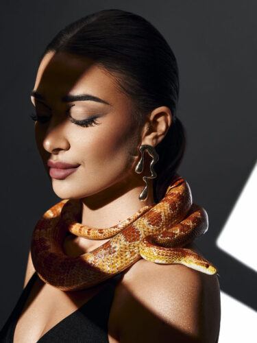 A dramatic studio portrait of a woman with a snake draped around her shoulders, showcasing bold, conceptual photography prompts to start the year strong.
