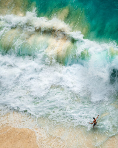 Person standing near crashing ocean waves viewed from above, showing the contrast between human scale and nature in Questmas 2025 by Tadej Cerkvenik.
