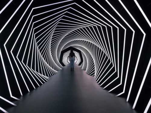 A person walks through a geometric tunnel of glowing white light lines, creating a futuristic scene that reflects movement, transition, and reflection in a year-in-review photography moment.