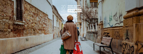 Street scene of a woman walking with shopping bags through a narrow alley, featured in the 500px Global Photography Awards 2025.