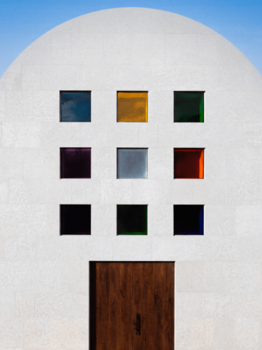 A minimalist building facade with evenly spaced square windows in different colors highlights repetition in photography and geometric design.